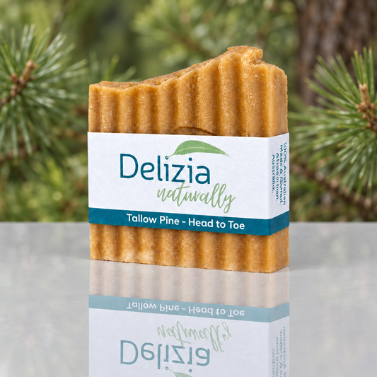 Delizia Naturally Tallow Pine Head to Toe soap bar with a teal-and-white label, reflected on a glossy surface against pine branches