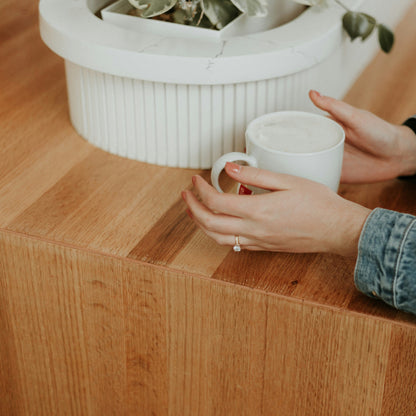 Person holding a white mug beside a timber benchtop