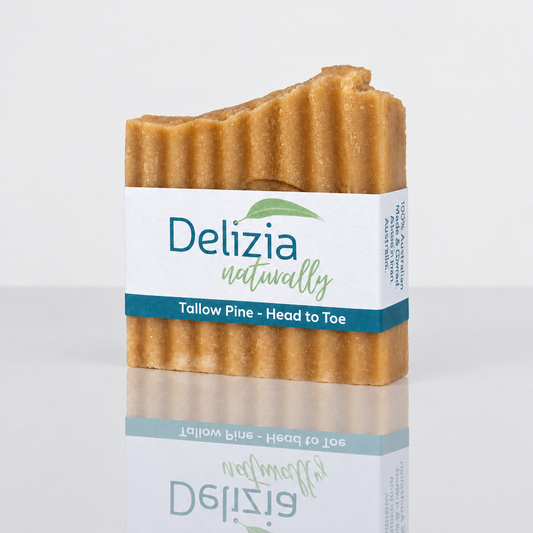 Delizia Naturally Tallow Pine Head to Toe soap bar with a ridged golden-brown surface and labelled paper wrap, shown with a mirror reflection